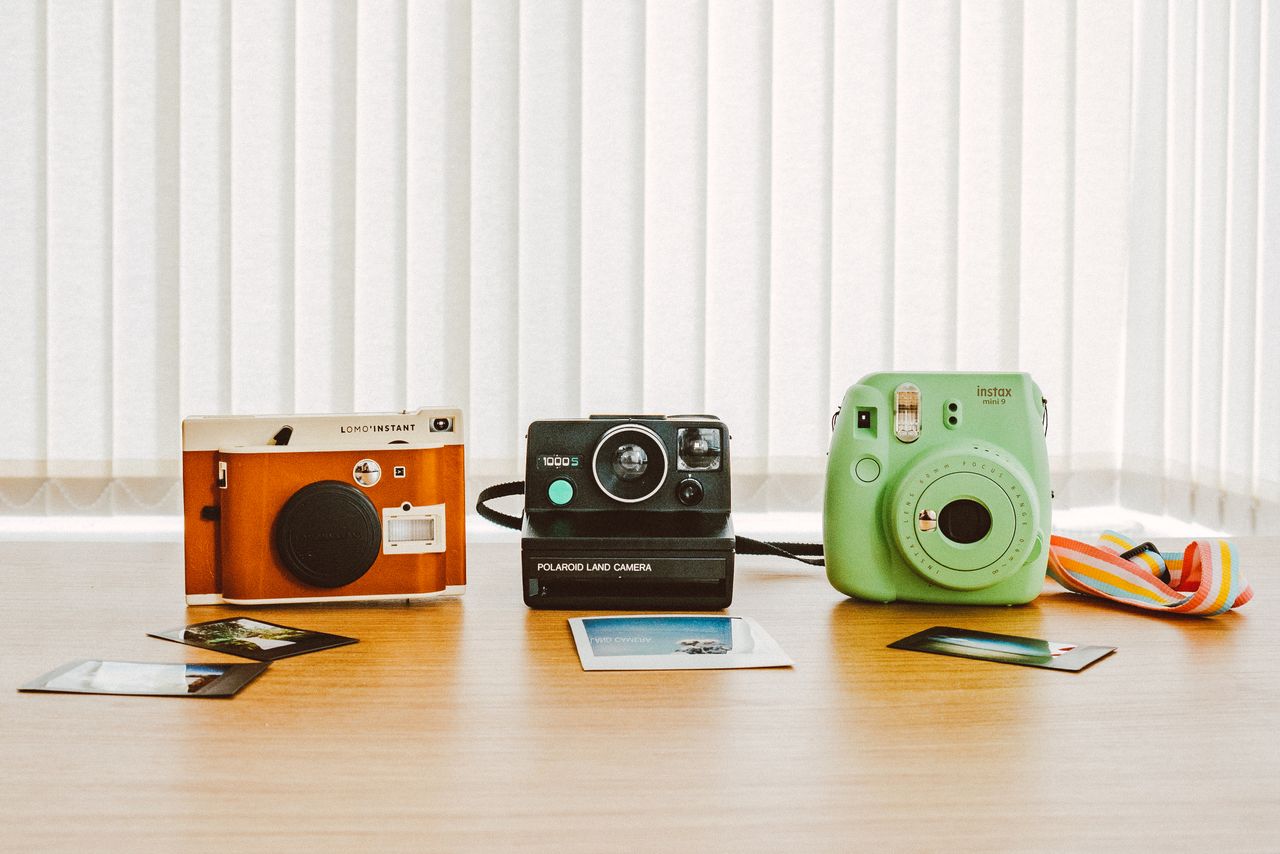 A collection of vintage and instant cameras on a wooden table with printed photos.