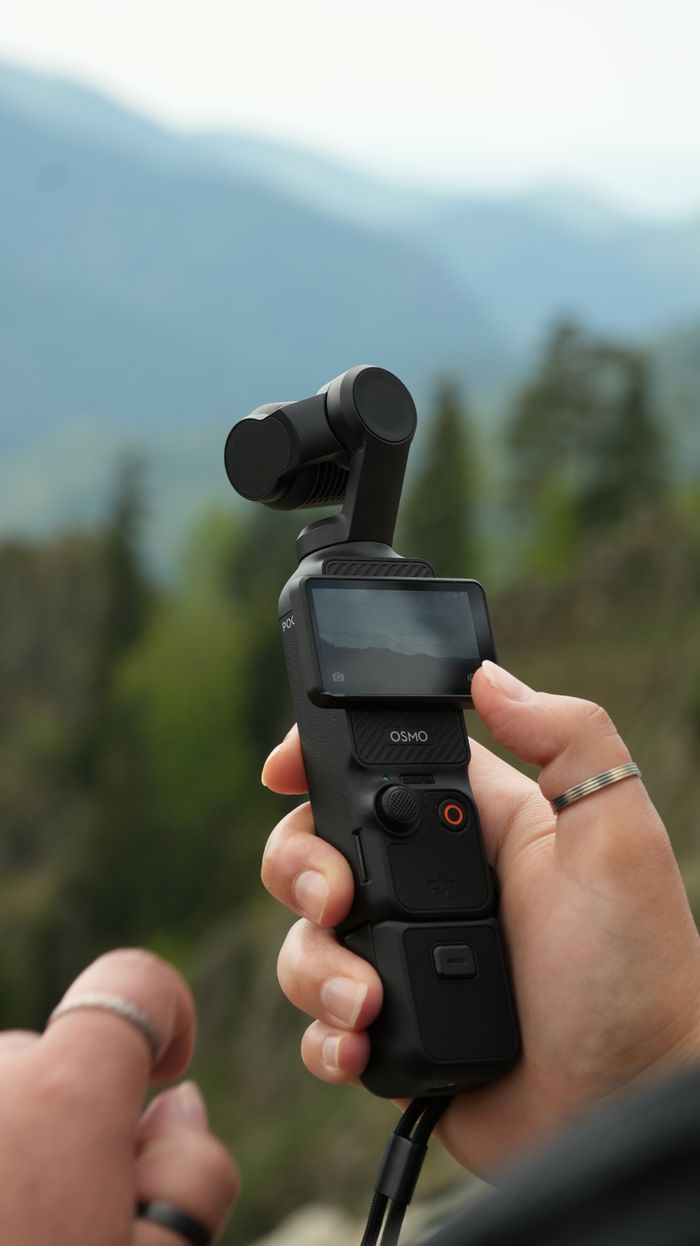 Close-up of a handheld gimbal camera with mountains in the background, ideal for travel and filming.